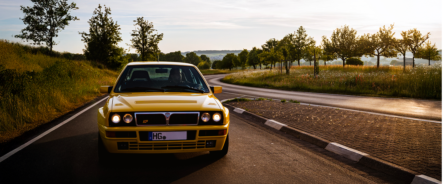 Gelber Lancia Delta Integrale fährt durch den Taunus im Sonnenuntergang